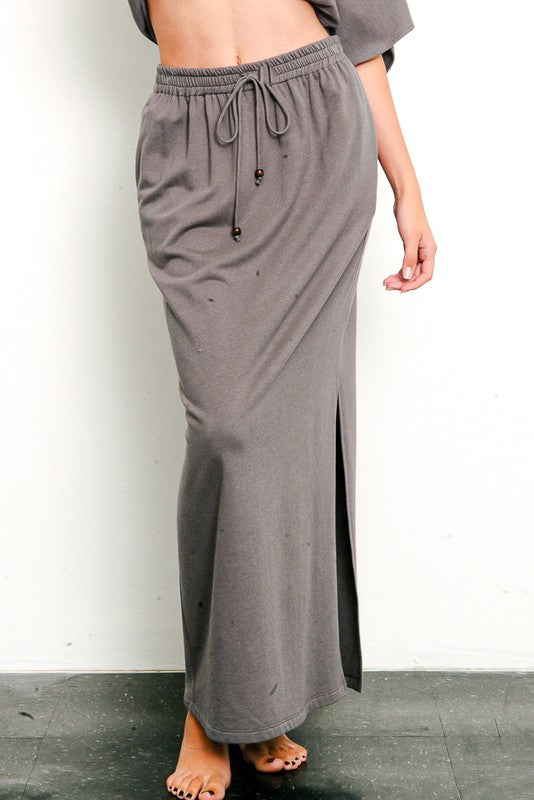 Model wearing a grey brushed organic hemp side slit maxi skirt against a white wall.