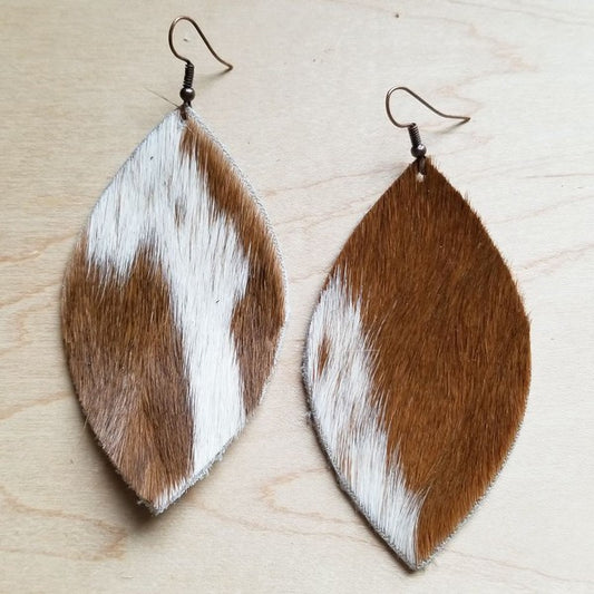 Oval shaped cow hide earrings in white and brown with a hook fastener on a wooden table.