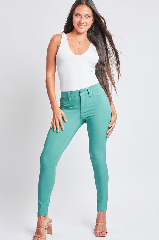 Model with long dark hair wearing a white tank top and mint green hyperstretch pants on a white backdrop.