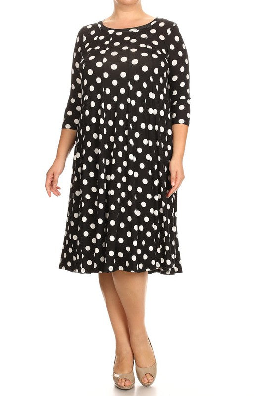 Model wearing a black relaxed fit dress with white polka dots that comes to the knee against a white backdrop.