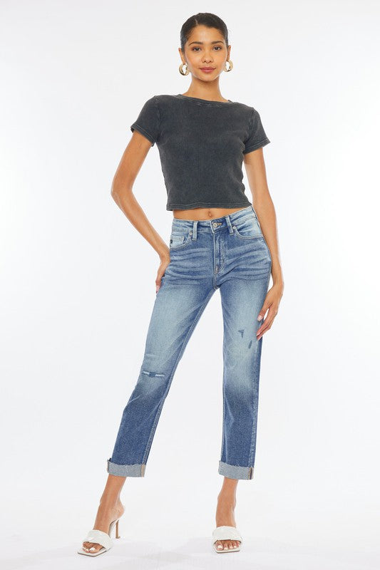 Model with dark hair wearing a black belly shirt and heels with mid blue high rise cuffed slim cut straight leg jeans.