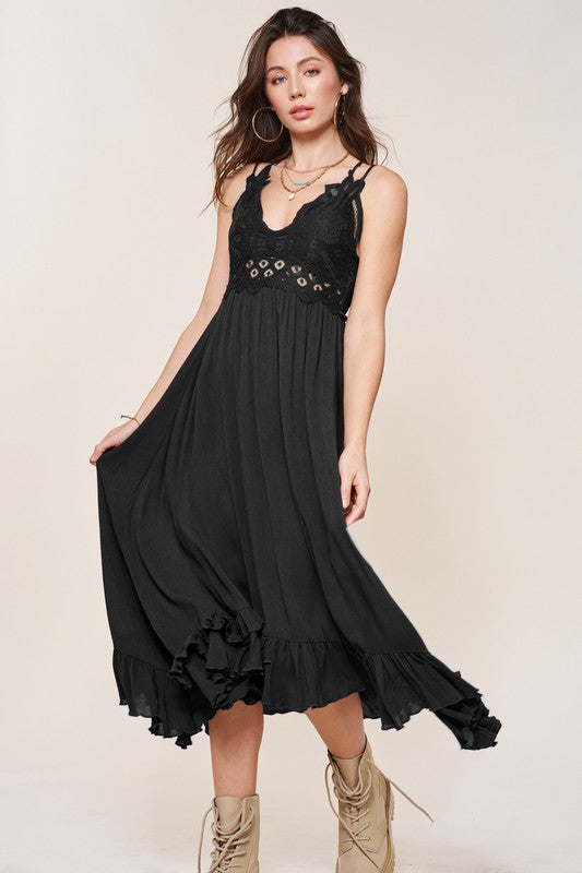 Brunette model wearing a long, midi-length slip dress with a crocheted top, full skirt, and ruffle hem in black.