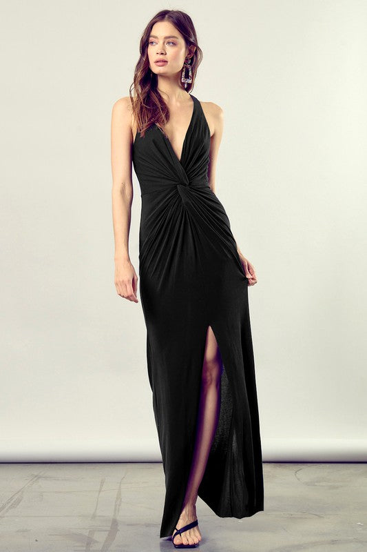 Brunette model wearing a twist front, deep-v neckiline, maxi dress in black jersey material with a leg slit.