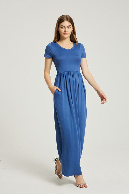 Brunette model wearing a blue casual maxi dress with an empire waist, short sleeves, and pockets in rayon.