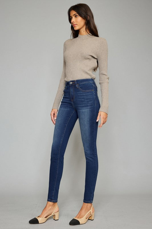 Brunette model wearing a tan sweater and black and tan slingbacks with high rise dark wash super skinny jeans.