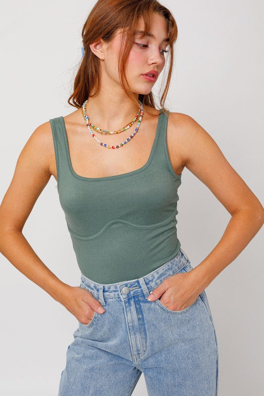 Redhead model wearing light color jeans with the sleeveless bodysuit in light olive against a white backdrop.