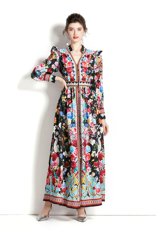 Brunette model wearinng a long-sleeve maxi dress with a v-neck, short collar, and ruffle shoulder detail in a vibrant floral print.