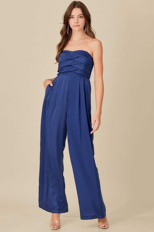 Brunette model wearing lazuli blue jumpsuit with overlapping top, strapless, with wide leg pants.