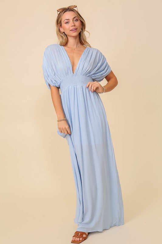 Blonde model against a soft yellow background wearing a rayon maxi dress with a smocked waist, gathered sleeve, and long loose bottom.