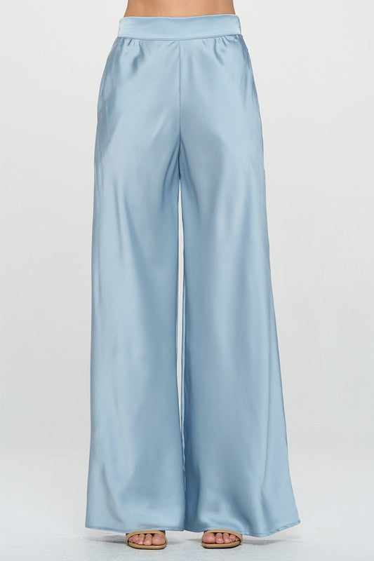 Model wearing light blue satin pants with elastic waist and side pockets against a white backdrop.