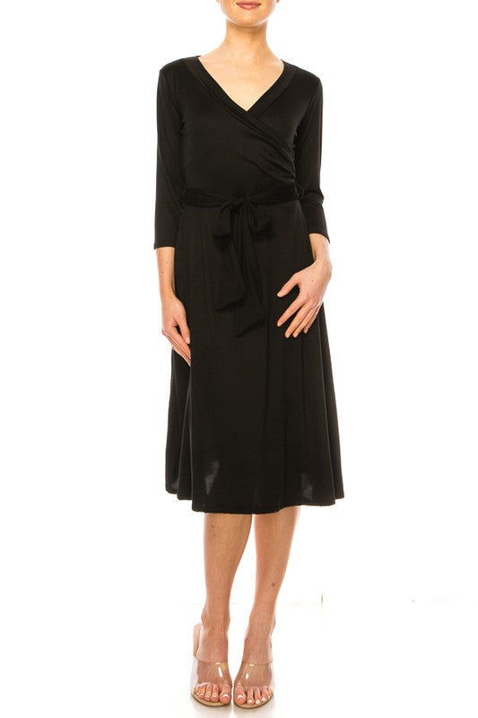 Model wearing faux wrap dress with v-neck in black with tie waist and 3/4 sleeves against a white backdrop.