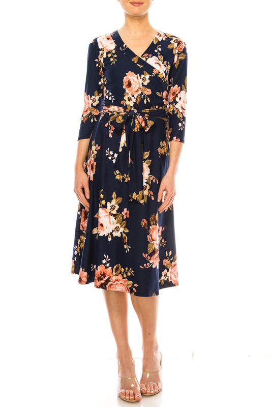 Model wearing navy and peach floral print faux wrap dress with 3/4 sleeves and tie waist in a rayon/spandex blend for comfort and durability.