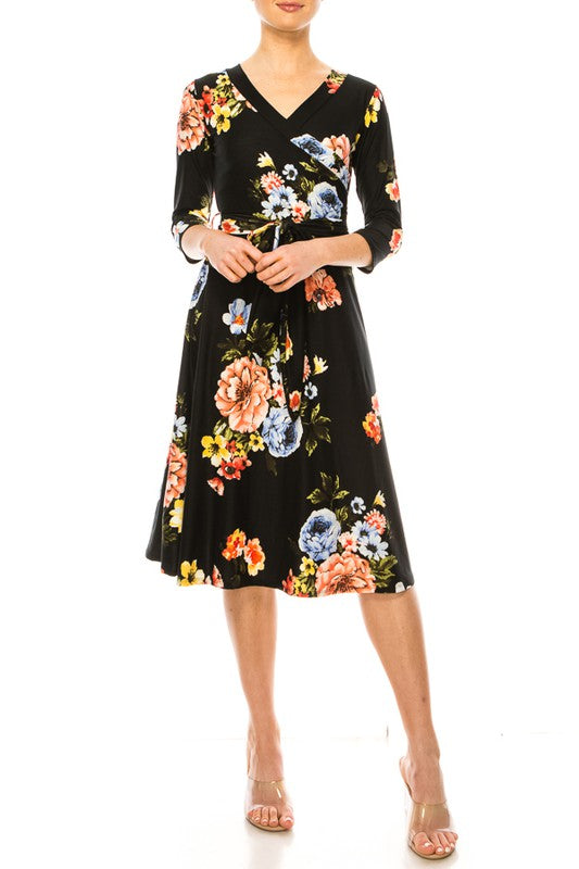 Model wearing a faux wrap dress with 3/4 sleeves and a tie belt. Black background with a blue, orange, and yellow floral print against a white backdrop.