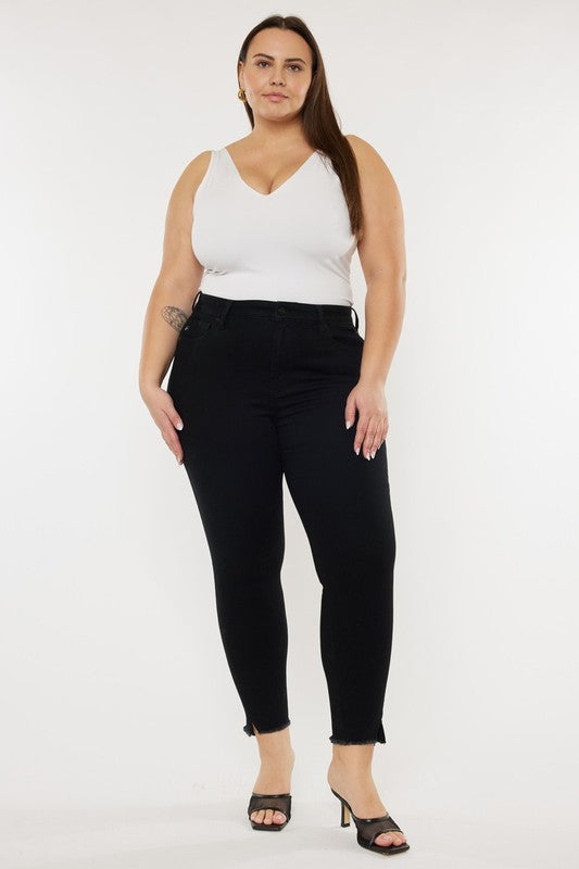 Plus size model wearing a white tank top and kitten heels with black plus size high rise ankle length skinny jeans with frayed hem.