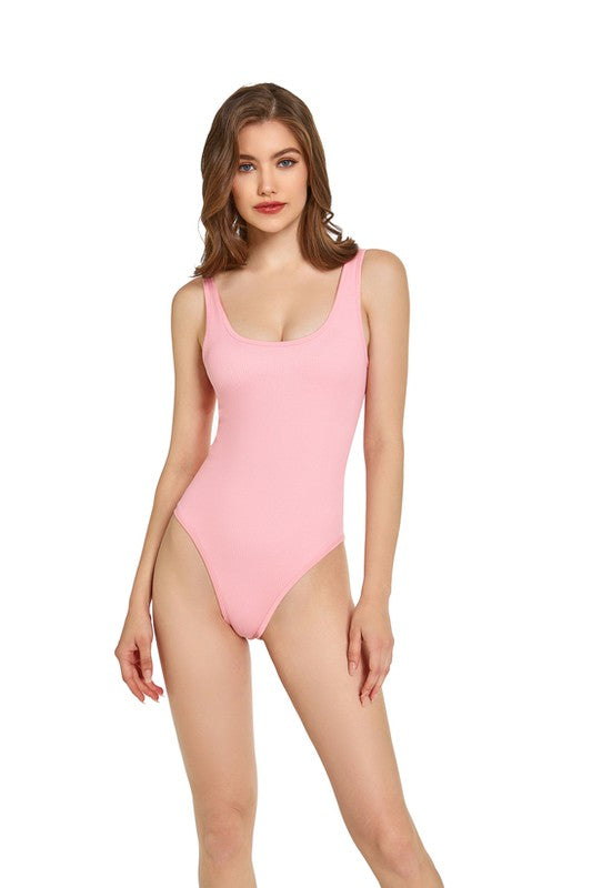 Brunette model wearing a seamless pink sleeveless bodysuit with a scoop neck against a white backdrop.