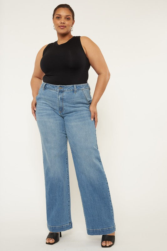 Plus size model with dark hair wearing black heels and a black tank top with plus high rise trouser wide leg jeans.