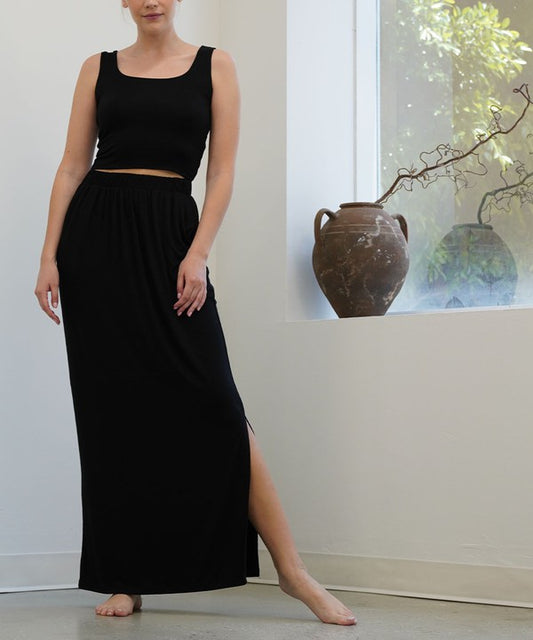 Model wearing a black tank top with a bamboo classic maxi skirt against a white wall and window.