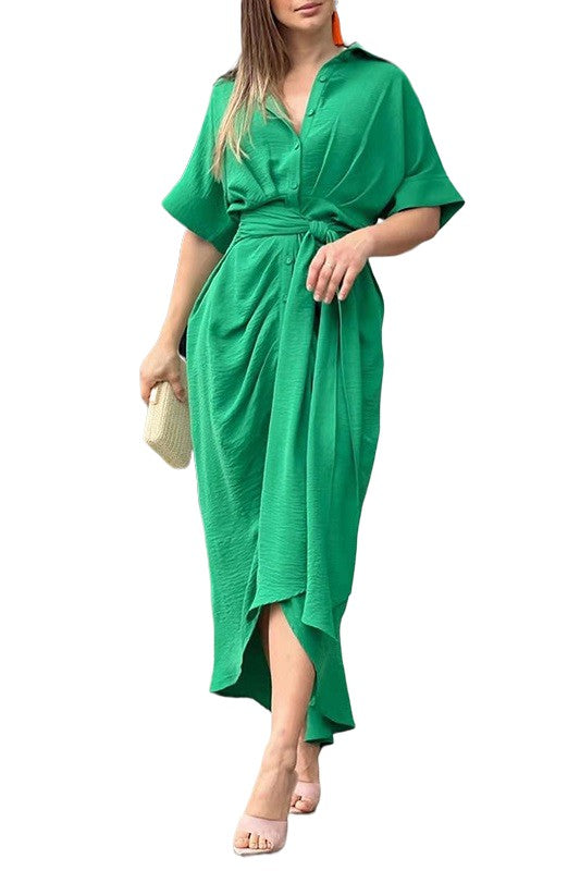 Blonde model wearing a green maxi shirt dress with short sleeves and a tie waist, made of a poly/cotton blend.