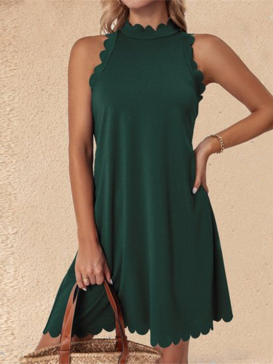 Blonde model wearing a flattering scalloped edge mock neck sleeveless mini dress in deep green. Available in other colors.