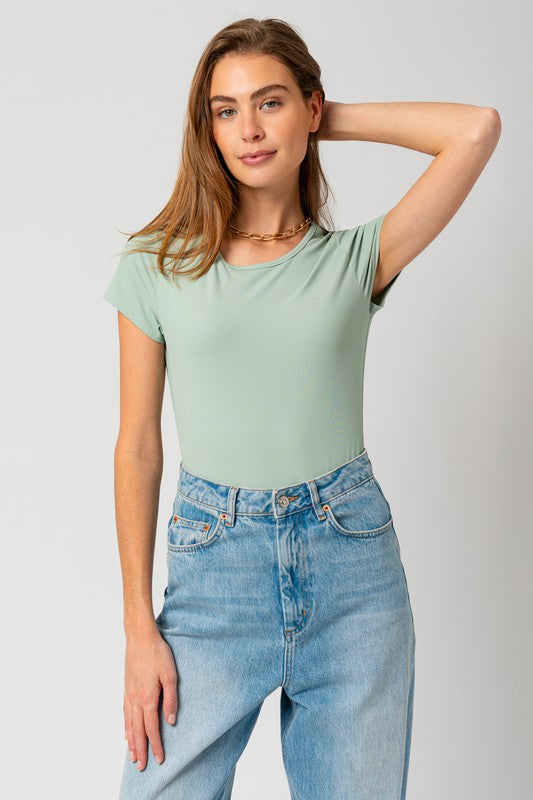 Model with brown hair wearing jeans with the round neck short sleeve bodysuit in green against a white backdrop.