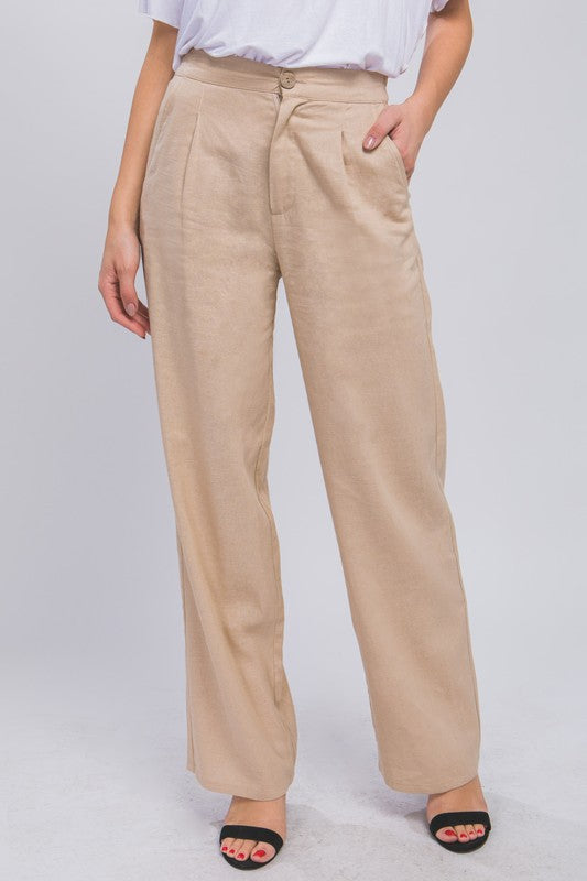 Beige linen blend pants with button waist and pleated front on a white backdrop.