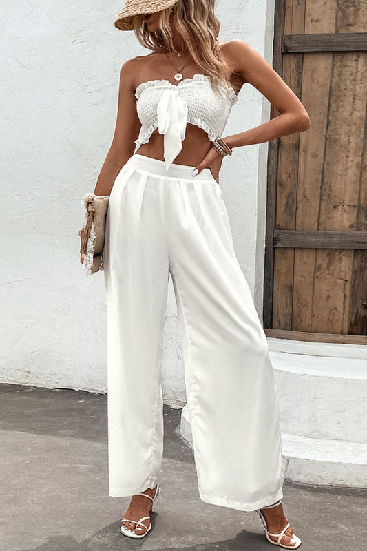 Blonde model in front of a white wall wearing a smocked tube top and wide leg pants set in bright white.