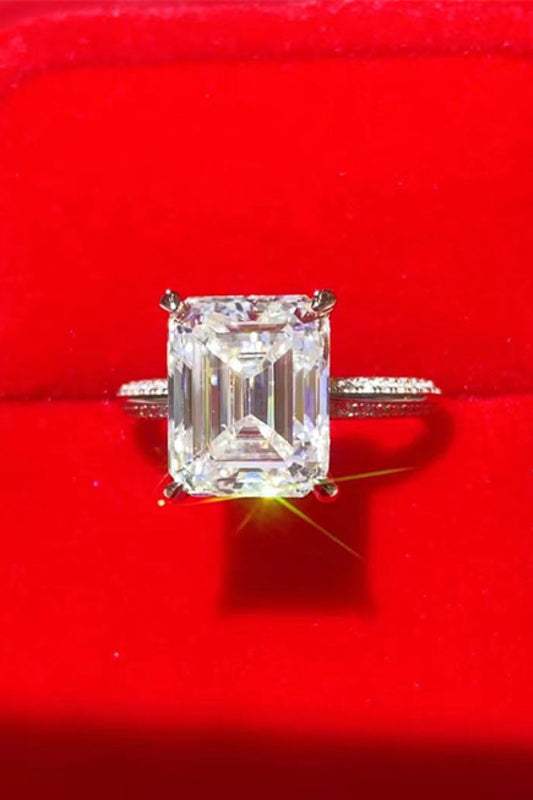 5-carat emerald cut moissanite ring set in platinum plated sterling silver pictured on a red background.