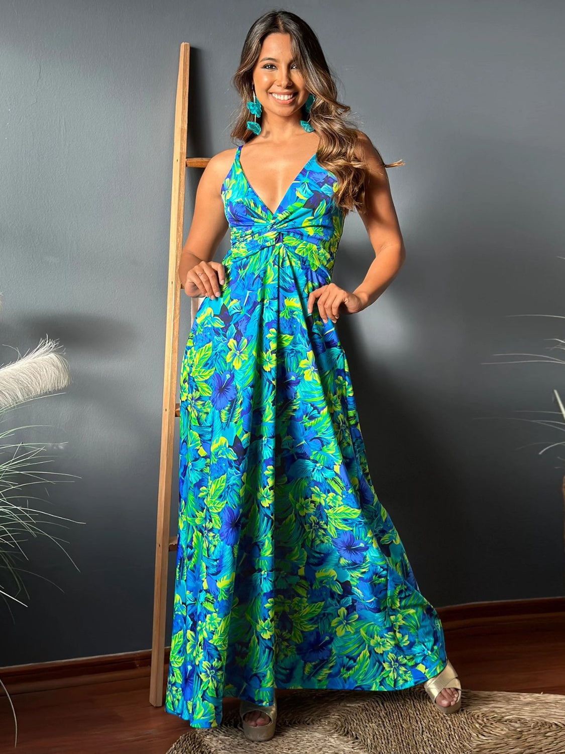 Brunette model wearing a blue, peacock, and lime floral tropical print maxi dress with a twist top, spaghetti straps, and wide maxi skirt. Available in many other colors and tropical prints.