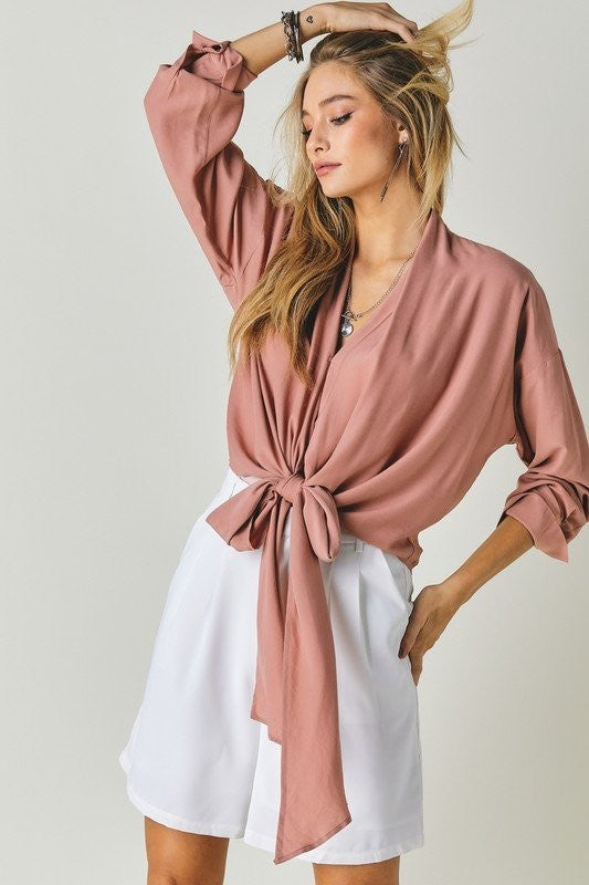 Blonde model wearing a long sleeve v neck bottom tie top in blush pink against a white backdrop.