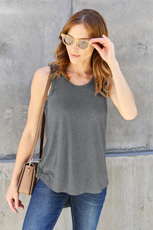 Redhead model wearing blue jeans and sunglasses with a heather grey loose fit round neck tank against a concrete wall.