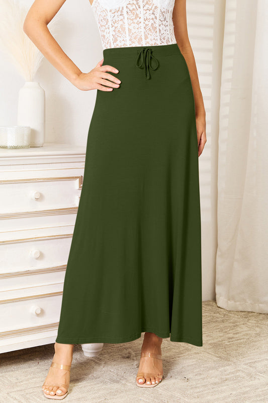 Model wearing a white corset and heels with the Double Take soft rayon drawstring waist maxi skirt in green in a white bedroom.