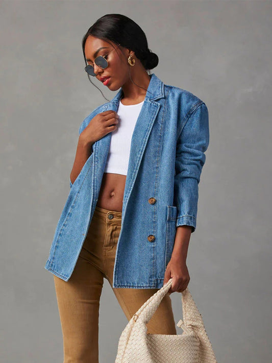 Model with dark hair wearing taupe jeans,, sunglasses and a white belly shirt with a collared, long sleeve two button denim blazer against a grey backdrop.