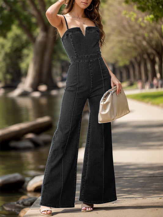 Brunette model standing next to a river wearing a black denim jumpsuit with wide legs, spaghetti straps, notched top and fitted waist.