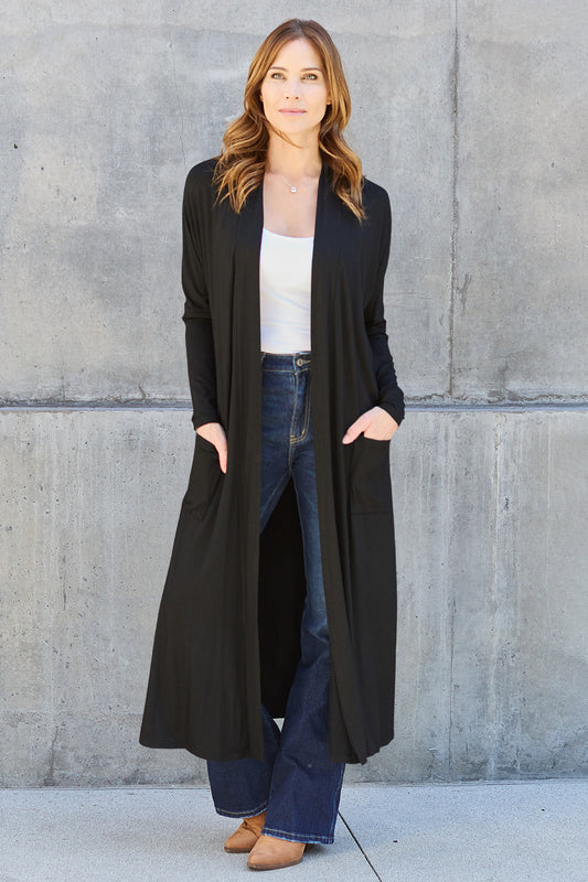 Model with red hair wearing boots, jeans and white shirt with an open front, long sleeve, ankle length cardigan in black.