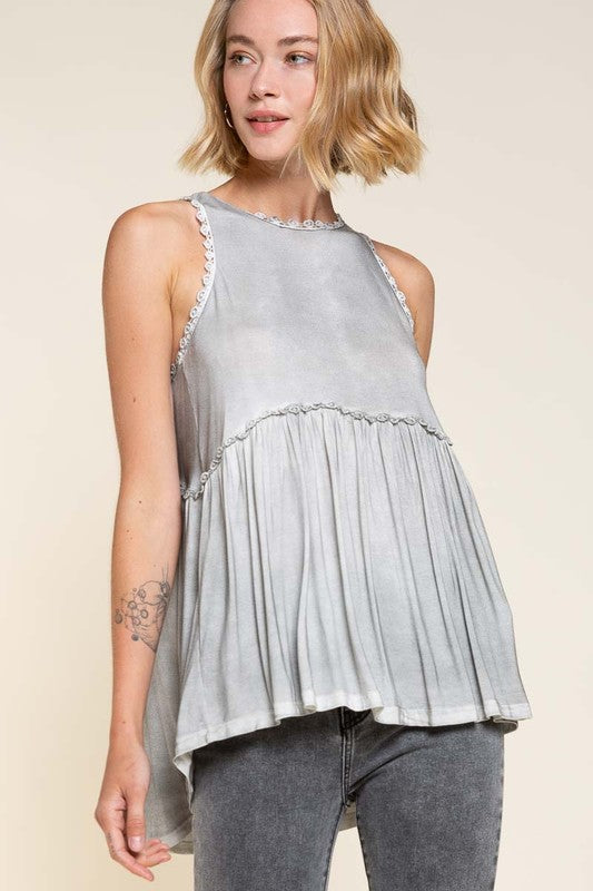 Babydoll tank top with lace edges, a racerback, and ruffles on a blonde model wearing grey jeans against an ecru backdrop.