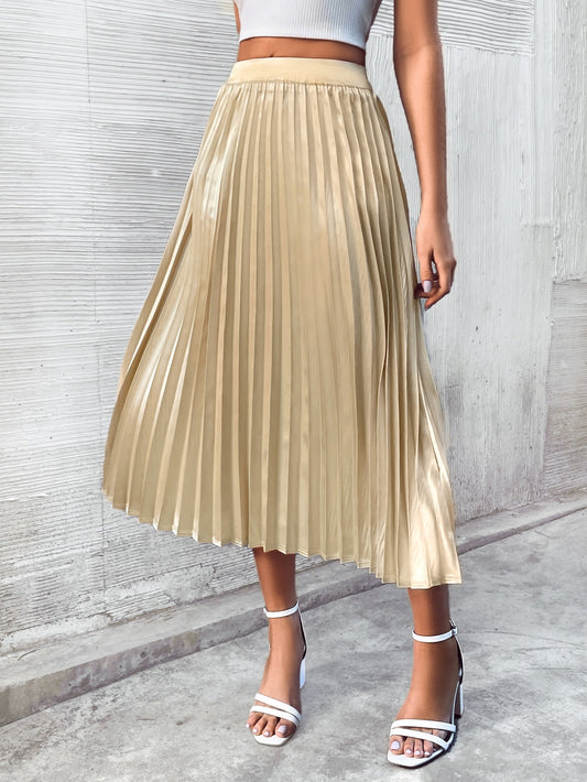 Model wearing a white crop top and heels with a cream pleated midi skirt with a gold finish in front of a concrete wall.