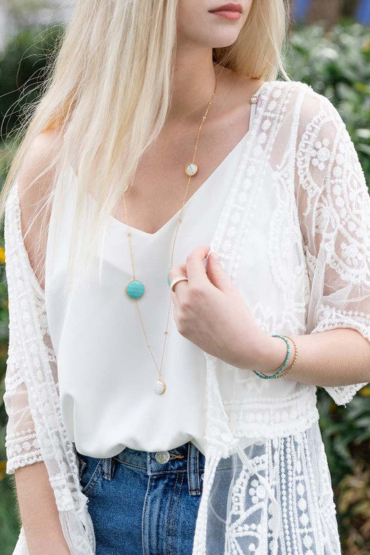 Blonde model wearing 36" gold plated necklace with one white stone at the bottom, two turqouise stones above, and two more white stones just below the collar bone. 