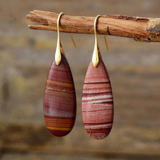 Red natural stone earrings with gold hooks, hanging on a tree branch.