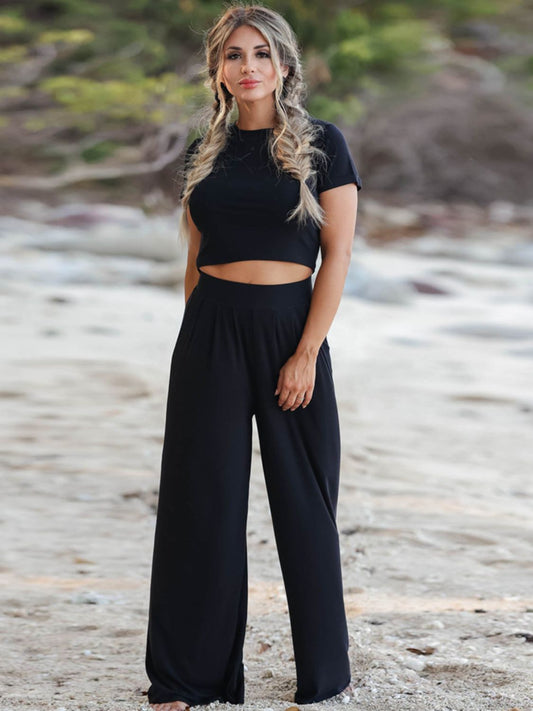 Blonde model on the beach wearing a black short sleeve cropped tee and wide leg pants set. Available in four colors.