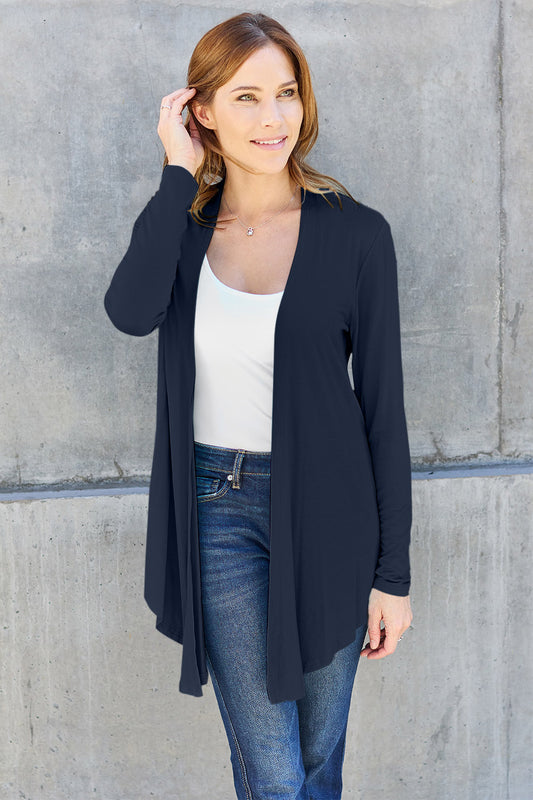 Model with red hair wearing a white top and blue jeans with an open front long sleeve soft rayon cardigan against a concrete wall.
