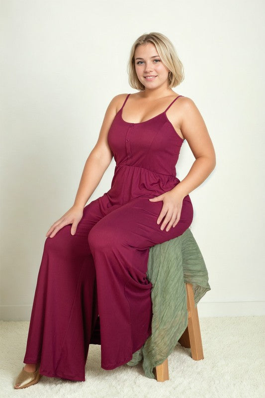 Blonde model wearing a bright pink jumpsuit with spaghetti straps, button front, and wide legs in front of a white backdrop.