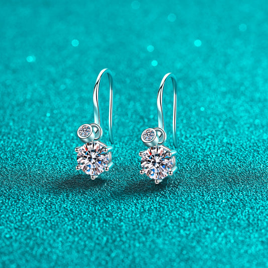 Pair of hook earrings with 1 carat Moissanite stone at the bottom of each hook, and a smaller stone above it, on a teal surface. Can be worn with smaller stone, only.