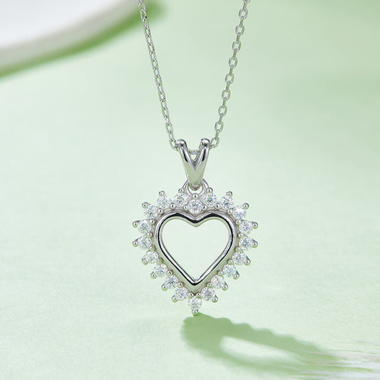 White gold over sterling silver Moissanite heart pendant necklace with Moissanite stones around the outer edge of the heart on a mint green surface.