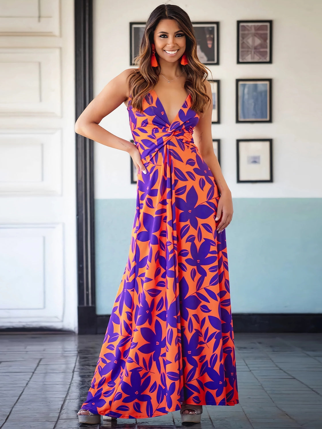 Brunette model wearing an orange and purple tropical print maxi dress with a twist top, spaghetti straps, and wide maxi skirt. Available in many other colors and tropical prints.