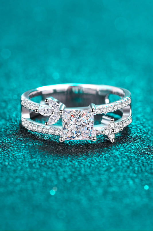 Double banded moissanite ring with a square center diamond, small accent diamonds around both bands, and larger accent stones placed on either side of the center. Photographed on a teal background.