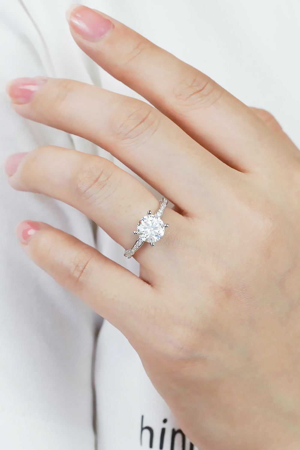 Model wearing a 1.5 carat round moissanite stone ring set in Platinum plated sterling silver with accent stones on the sides of the band.