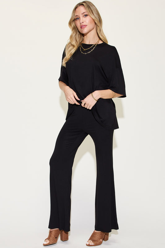 Blonde model in front of white backdrop wearing a two-piece bamboo clothing set of a black loose fit drop shoulder tee and elastic waist flare pants, also in black. Available in pink, chocolate, and mint.