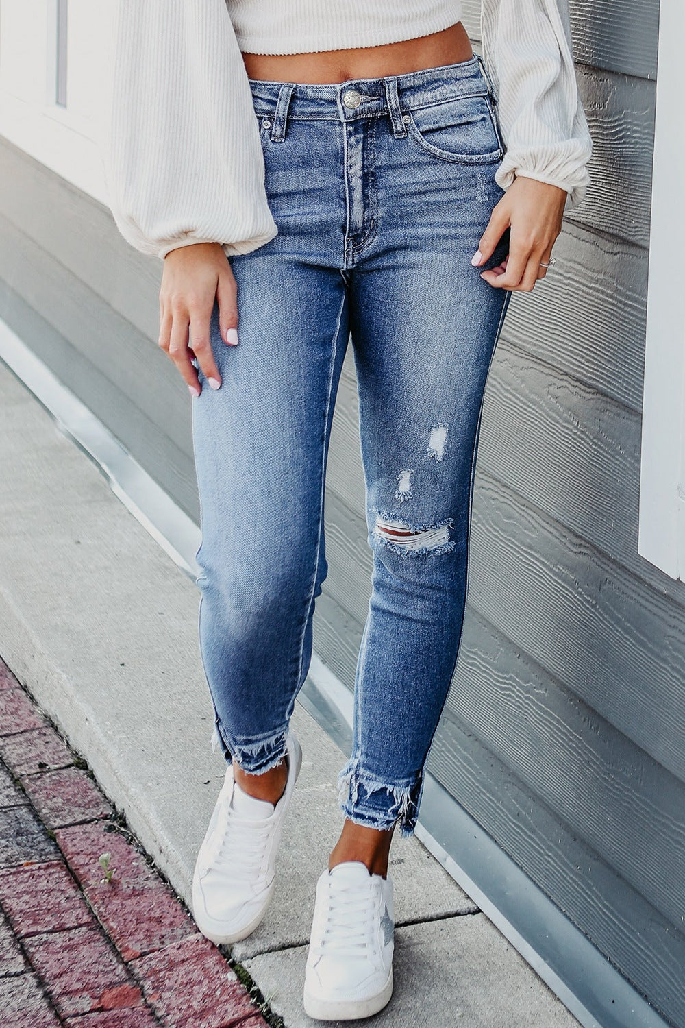 Model wearing a white top with SYNZ raw hem, distressed skinny jeans with pockets in medium blue.