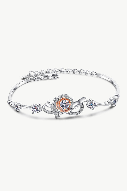 Delicate 1.5 carat rhodium plated sterling silver adjustable bracelet with four small Moissanite stones to the sides and one larger Moissanite stone in the center, set in a rose gold flower. Photographed on a white background.