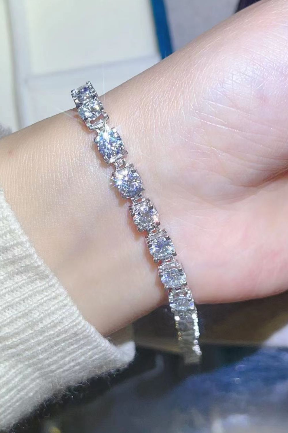 Classic 10 carat Moissanite tennis bracelet set in platinum plated sterling silver on a model wrist wearing a white sweater.